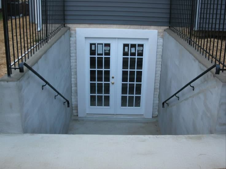 Finished basement entrance with white French doors and railings